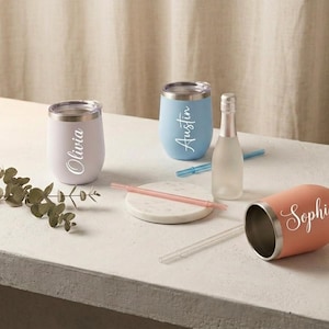May include: Three stainless steel tumblers in light pink, light blue, and coral, each featuring a white script name: Olivia, Austin, and Sophia. The set includes a small glass bottle, two clear plastic straws, and a round white marble coaster.