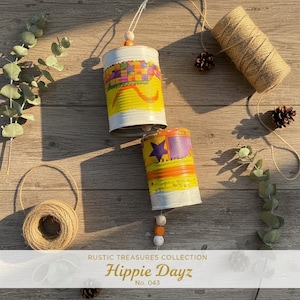 May include: Two cylindrical metal cans decorated with colourful painted patterns including purple stars and orange wavy lines. Each can features a wooden bead accent and is suspended by twine. The text "RUSTIC TREASURES COLLECTION Hippie Dayz No. 043" is visible at the bottom.