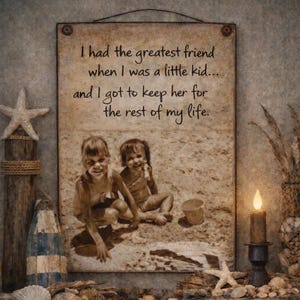 May include: A framed sepia-toned print with the text "I had the greatest friend when I was a little kid... and I got to keep her for the rest of my life." The print features a photo of two young girls on a beach. Decorative elements include a starfish, shells, and a lit candle.