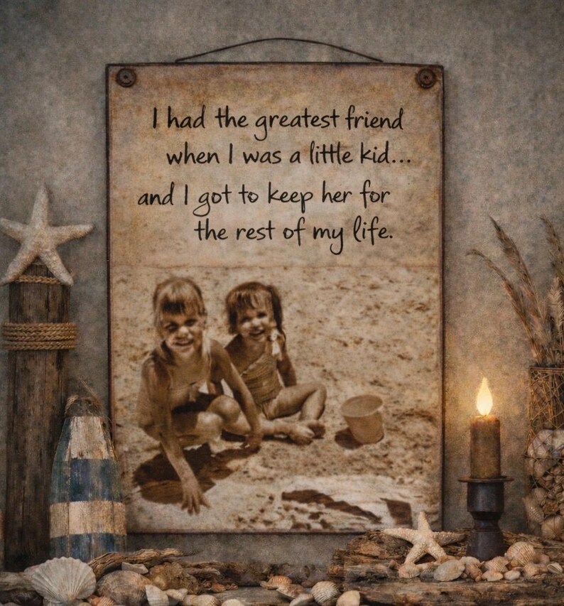 May include: A framed sepia-toned print with the text "I had the greatest friend when I was a little kid... and I got to keep her for the rest of my life." The print features a photo of two young girls on a beach. Decorative elements include a starfish, shells, and a lit candle.