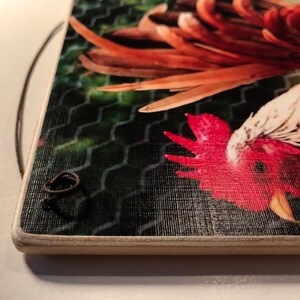 May include: A rectangular wooden sign featuring a rooster illustration. The rooster has red, white, and brown feathers, set against a green mesh background. A dark brown string is attached for hanging.