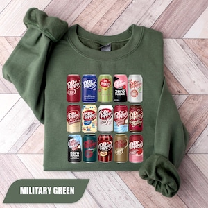 May include: A military green crewneck sweatshirt featuring a graphic print of fifteen different Dr Pepper soda cans arranged in a grid. The cans display various colors and labels including Dr Pepper, Diet, Zero Sugar, and Cream Soda varieties.