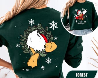 Könnte beinhalten: Ein waldgrüner Rundhals-Pullover mit einer Grafik auf der Rückseite von Donald Duck mit Weihnachtsmütze in einem grünen Kranz mit weißen Schneeflocken. Die Vorderseite zeigt Donald Duck mit dem Schriftzug 'Tis The Season'.
