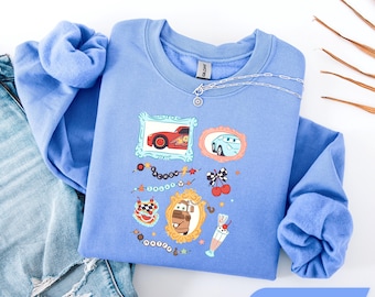 Könnte beinhalten: Ein Carolina-blaues Sweatshirt mit Rundhalsausschnitt und einem Grafikdruck von Charakteren aus dem Film Cars. Das Design zeigt gerahmte Illustrationen von Lightning McQueen, Sally und Hook sowie kleine Symbole wie Kirschen und einen Milchshake.