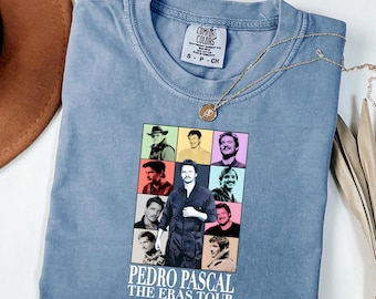 Könnte beinhalten: Ein kurzärmeliges T-Shirt in Jeansblau mit einem Grafikdruck von Pedro Pascal in verschiedenen Rollen, angeordnet in einem Raster. Unter dem Raster steht der Text "PEDRO PASCAL THE ERAS TOUR" in weißen Großbuchstaben.