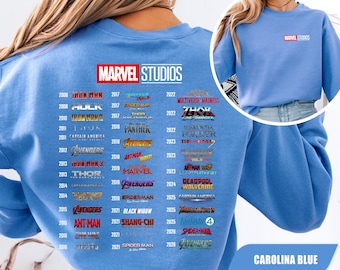 Könnte beinhalten: Ein hellblaues Sweatshirt mit Rundhalsausschnitt, das auf der Rückseite das Marvel Studios Logo und eine chronologische Liste von Filmtiteln von 2008 bis 2026 zeigt. Auf der Vorderseite befindet sich ein kleineres Marvel Studios Logo.