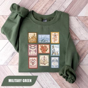 Peut inclure: Un sweat-shirt à col rond vert olive orné d'un imprimé graphique composé de neuf motifs rectangulaires en forme de timbres-poste. Les timbres présentent diverses illustrations dont un château, une montagne, une épée, des roses et des ailes.