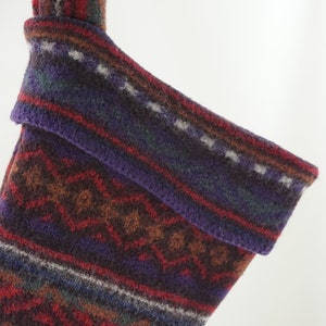 May include: A colorful knitted stocking with a geometric pattern in shades of red, brown, purple, and gray.