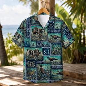 Puede incluir: Una camisa de manga corta con botones y un patrón de patchwork en tonos azul y verde azulado. El diseño incluye ilustraciones de perros de caza y faisanes en campos de hierba, intercaladas con motivos geométricos y circulares en la tela.