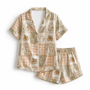 Puede incluir: Un conjunto de pijama de camisa de manga corta con botones y pantalón corto a juego, con un patrón de patchwork de cuadros vichy naranja claro, estampados florales verde salvia e ilustraciones de fantasmas blancos y calabazas naranjas.