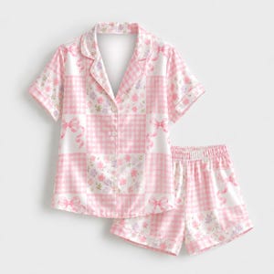 May include: A short-sleeve button-down pajama shirt and matching shorts set featuring a patchwork pattern of pink gingham squares and white squares with pink ribbons and small purple and pink floral clusters on a white background.