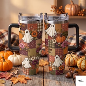 May include: Two stainless steel tumblers with black handles and clear lids, featuring a patchwork design of ghosts, orange pumpkins, and autumn flowers in shades of brown, orange, and cream. The pattern includes plaid and polka dot squares.