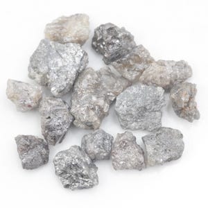 Peut inclure: Une collection de diamants bruts et non taillés dans diverses nuances de gris, d'argent et de blanc cassé. Ces pierres naturelles présentent des formes irrégulières et dentelées avec des surfaces cristallines qui reflètent la lumière.