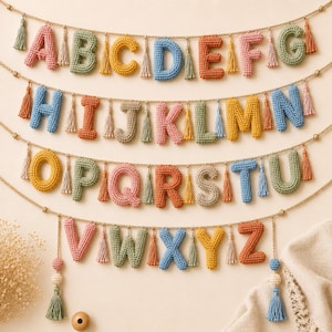 Könnte beinhalten: Ein mehrreihiger Wandbehang mit einzelnen gehäkelten Buchstaben des Alphabets von A bis Z. Jeder Buchstabe ist in verschiedenen Farben wie Rosa, Grün, Gelb, Blau und Orange gefertigt und an einem Seil mit kleinen Quasten befestigt.