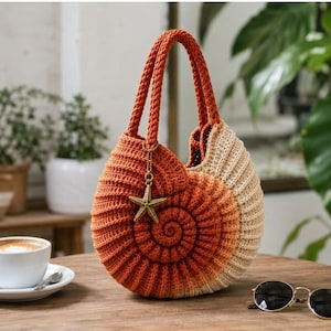 May include: A round crochet handbag shaped like a nautilus shell, featuring a gradient colour pattern transitioning from deep orange to light beige. The bag has two braided handles and a gold-toned metal starfish charm attached to one handle.