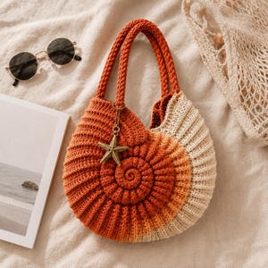 May include: A spiral-shaped crochet handbag featuring an ombre colour gradient transitioning from deep orange to light cream. The bag has two braided handles and a gold-toned starfish charm attached to one handle, mimicking the form of a seashell.