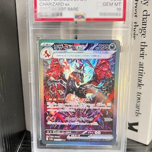 Può includere: Una carta collezionabile Pokemon SV4a JP Charizard ex del 2023, certificata PSA e racchiusa in una custodia di plastica trasparente. La carta presenta un'illustrazione olografica di un drago scuro con ali rosse, testo giapponese e 330 HP.