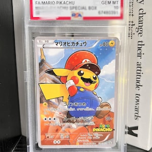 May include: A 2016 P.M. JPN. XY Promo #294 Mario Pikachu trading card graded GEM MT 10 by PSA. The card features a yellow Pikachu character wearing a red Mario hat and blue overalls with a moustache, set against a background of a Japanese castle.