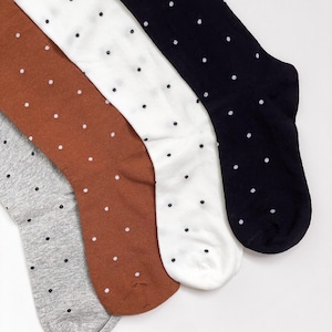 May include: A set of four pairs of socks featuring a polka dot pattern. The socks are available in black, white, rust orange, and heather gray, each decorated with small, evenly spaced white dots across the entire surface of the fabric.
