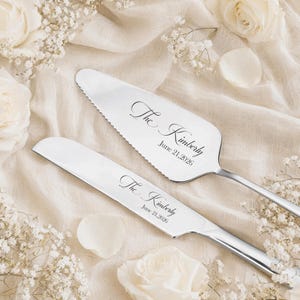 May include: A silver-toned cake knife and server set featuring a serrated edge on the server. Both pieces are engraved with the script text The Kimberly and the date June 21, 2026, in a clean, elegant font style on the polished metal surfaces.