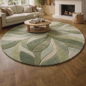 May include: A large, circular area rug featuring a tufted, abstract leaf pattern in various shades of sage green, olive, and cream. The rug has a textured, carved pile design with curved, organic shapes that flow across the entire surface.