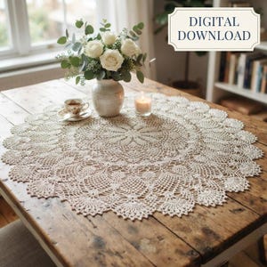Op de afbeelding: Een rond, crèmekleurig gehaakt kleedje met een ingewikkeld bloemenpatroon ligt op een houten tafel. Een witte keramische vaas bevat witte rozen en groene eucalyptusbladeren. Een klein theekopje en een brandende kaars staan in de buurt. Digitale download.