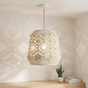 May include: A cream-colored macrame pendant light fixture featuring an intricate diamond-shaped knotted pattern with small decorative beads. The cylindrical shade hangs from a single cord attached to a white circular ceiling mount.
