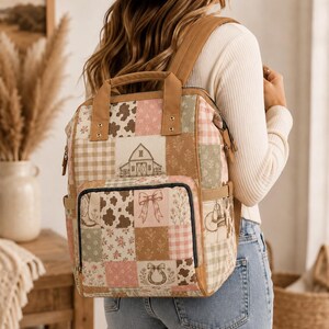 Puede incluir: Una mochila con diseño de patchwork que presenta varios patrones, incluyendo manchas de vaca, cuadros vichy, motivos florales, una ilustración de granero, botas vaqueras, lazos y herraduras en tonos beige, rosa y verde salvia con ribetes marrones.