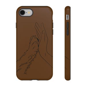 May include: A brown smartphone case featuring a black line art illustration of a human hand giving a high-five to a furry animal paw. The design is centred on the back of the case, which includes cutouts for the camera lens and flash.