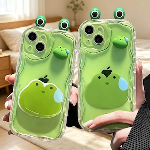Può includere: Due cover trasparenti per telefono con bordo ondulato, sfondo verde chiaro e grafica a forma di rana. Ogni cover presenta due piccoli occhi di rana che sporgono dalla parte superiore e una piccola figura di rana 3D applicata sul retro.