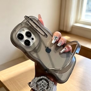 May include: A translucent dark gray smartphone case with a raised, wavy-edged frame and a cutout for the triple-lens camera system. The case features a smooth, semi-transparent finish that reveals the Apple logo on the back of the device.
