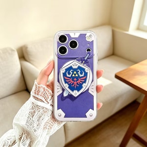May include: A clear smartphone case featuring a purple background with a graphic of a blue and silver shield and a sword. The shield displays a red bird emblem and a yellow triangular symbol. The case has cutouts for the camera lenses and flash.
