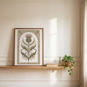 Könnte beinhalten: Ein rechteckiger gerahmter Druck mit einer detaillierten botanischen Illustration einer Distelpflanze in Grün- und Goldtönen, eingefasst in einen verzierten, bogenförmigen dekorativen Rahmen auf weißem Hintergrund, präsentiert in einem dunklen Holzrahmen.