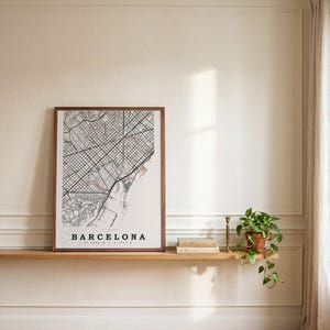 May include: A framed rectangular wall art print featuring a detailed black and white street map of Barcelona, Spain. The print includes the text BARCELONA and geographic coordinates at the bottom, encased in a simple dark brown wooden frame.