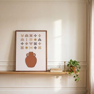 Può includere: Una stampa artistica incorniciata raffigurante un'anfora color terracotta centrata in basso, sormontata da una griglia di vari simboli geometrici, tra cui arcobaleni, soli e rombi in tonalità marrone, giallo senape e nero.