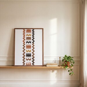 May include: A rectangular framed wall art piece featuring a vertical column of abstract geometric shapes and zigzag patterns in shades of terracotta, mustard yellow, brown, and black on a white background, enclosed in a dark wood frame.
