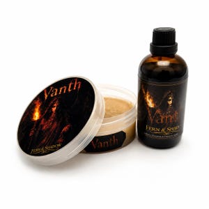 May include: A round plastic container with a beige substance and a matching lid, alongside a dark amber glass bottle with a black cap. Both items feature labels with the text Vanth and Fern & Shadow, depicting a figure holding a torch.