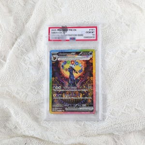 Op de afbeelding: Een gegradeerde Umbreon EX ruilkaart in een doorzichtige plastic houder. De kaart toont een donker, gestileerd wezen met kleurrijke cirkelvormige accenten en de tekst Moon Mirage en Onyx. Het label bovenaan vermeldt 2025 POKEMON PRE EN UMBREON #161 GEM MT 10.