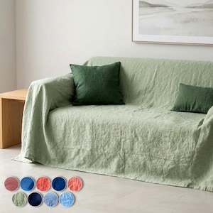 May include: A light sage green sofa cover draped over a couch, featuring two dark forest green throw pillows. Below the sofa, ten circular fabric swatches are displayed in various colours including pink, blue, orange, and green shades.