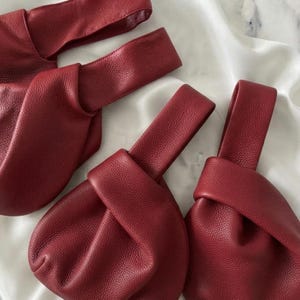 K&ouml;nnte beinhalten: Drei dunkelrote Handtaschen aus strukturiertem Leder. Jede Tasche verf&uuml;gt &uuml;ber einen einzelnen integrierten Griff, der durch den Hauptk&ouml;rper verl&auml;uft und eine geraffte, weiche Silhouette erzeugt. Die Lederoberfl&auml;che weist eine deutliche Narbung auf.