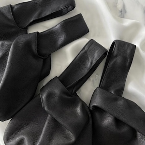 K&ouml;nnte beinhalten: Drei schwarze Handtaschen mit strukturierter Oberfl&auml;che und einem geknoteten Griffdesign. Jede Tasche verf&uuml;gt &uuml;ber einen durchgehenden Riemen, der durch den K&ouml;rper der Tasche verl&auml;uft und eine geraffte, weiche Silhouette mit einer genarbten Textur erzeugt.