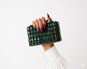 May include: A rectangular clutch bag covered in a grid of emerald green rectangular crystals set in a gold-toned metal frame. The bag features a structured design with a repeating pattern of faceted green stones across the entire front surface.