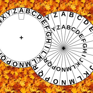 May include: A white circular cipher wheel featuring the alphabet printed in black around the outer edge. The wheel has a central plus sign and a small rectangular cutout near the top. The design is displayed against a background of orange autumn leaves.