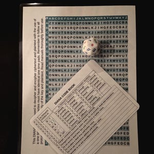 Puede incluir: Un dado blanco de veinte caras con letras de colores sobre una hoja impresa con una cuadrícula de letras y una tarjeta Diana Code Book. La tarjeta contiene tablas de códigos alternativos, palabras de diccionario e instrucciones de cifrado.