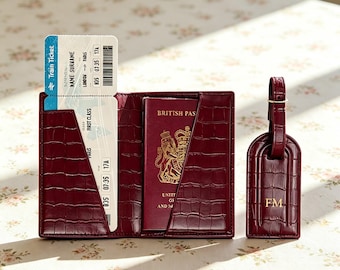 Puede incluir: Un portapasaportes de cuero color burdeos con relieve de cocodrilo que contiene un pasaporte británico y un billete de tren de Londres a París, junto con una etiqueta de equipaje a juego con las iniciales FM grabadas en oro.