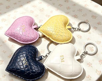 Puede incluir: Cuatro llaveros en forma de corazón con un patrón texturizado de piel de cocodrilo. Los llaveros son de color rosa, amarillo, azul oscuro y blanco. Cada corazón presenta iniciales doradas en relieve: IM en el rosa, NY en el azul oscuro y EM en el blanco. Cada uno incluye una anilla de metal plateado.