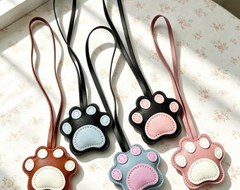 Puede incluir: Cinco colgantes de cuero con forma de pata y correas largas. Los colgantes presentan varias combinaciones de colores, incluyendo marrón con blanco, negro con azul claro, negro con rosa, azul claro con rosa y rosa con blanco, con costuras.