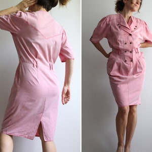 May include: A pink short-sleeved dress with a button-up front and a cinched waist. The dress has a slightly puffed sleeve and a skirt that falls to the knee.