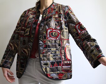 May include: A quilted jacket with a geometric pattern in shades of red, black, green, and gold. The jacket has a stand-up collar and a zipper closure.