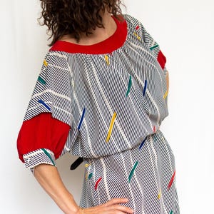 May include: A white and blue striped dress with red sleeves and colorful geometric patterns. The dress has a gathered neckline and a fitted waist.
